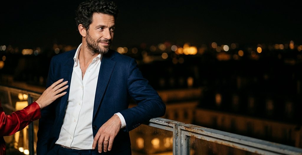 Homme marié en déplacement sur le balcon d’un hôtel la nuit, une femme pose la main sur son bras