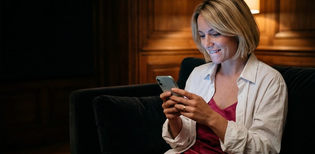 Femme mariée qui sourit en tchattant avec un homme sur son téléphone, installée dans un canapé